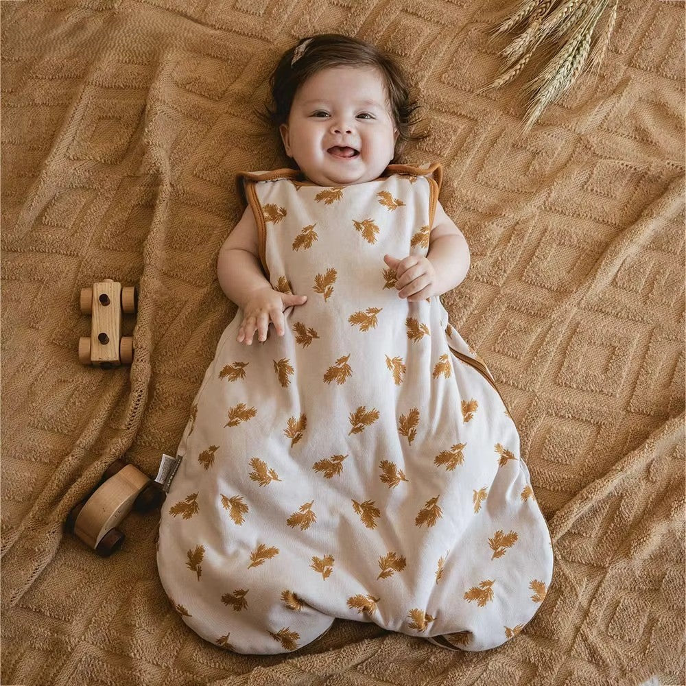 Bébé souriant dans gigoteuse beige motifs feuilles dorées coton doux