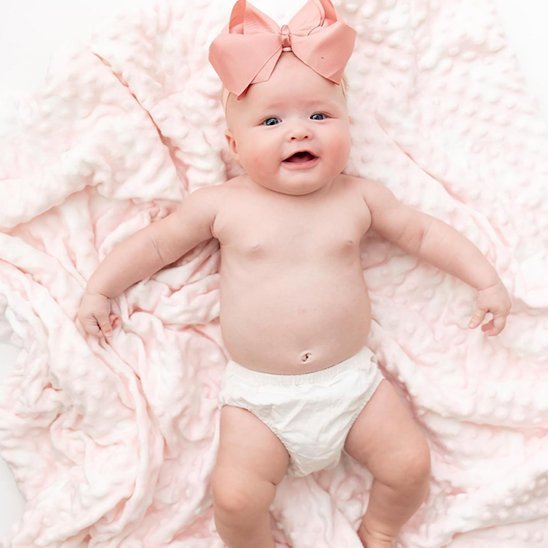 Bébé fille souriante avec nœud rose sur couverture bébé rose douce