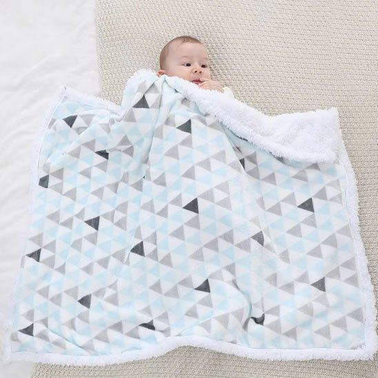 Bébé en vêtements blancs allongé sur couverture géométrique triangulaire bleu et gris, démonstration de la taille et du confort