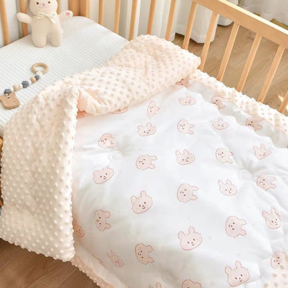 Couverture réversible lapin rose bébé et minky rose clair  joliment disposée dans un berceau.