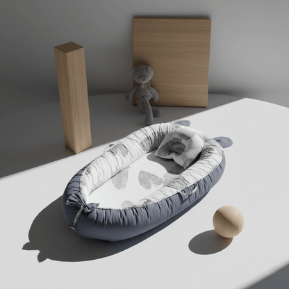 Réducteur de Lit Bébé-Cocon Motif Feuillages - Nid portable avec motifs botaniques gris sur fond blanc, bordures bleues, parfait pour chambre moderne et décoration scandinave